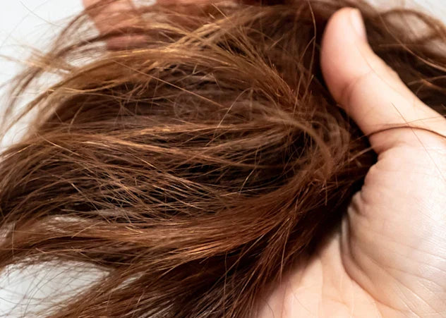 Fair-skinned hand running through dry tangled brown hair on white background illustrating need for moisturizing conditioner