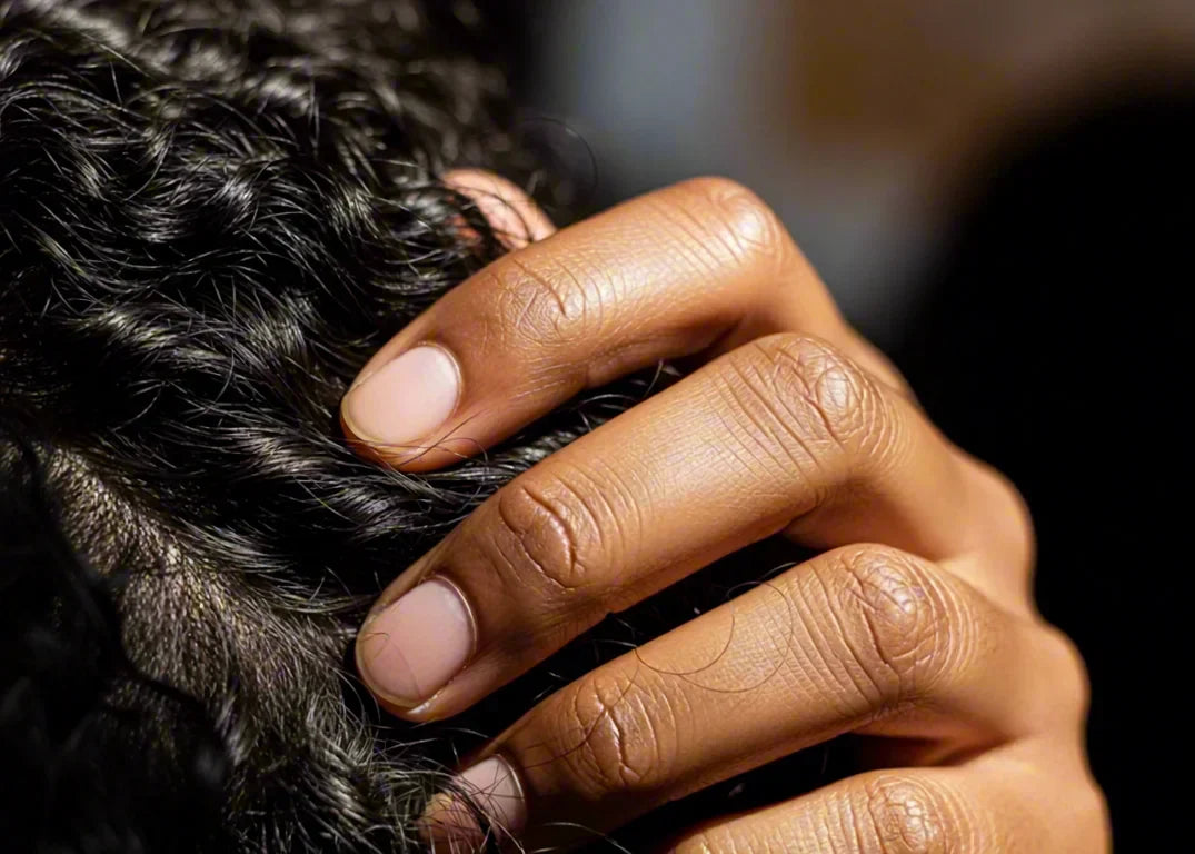 Dark-skinned woman's hand touches her black thinning hair in front of a brown background