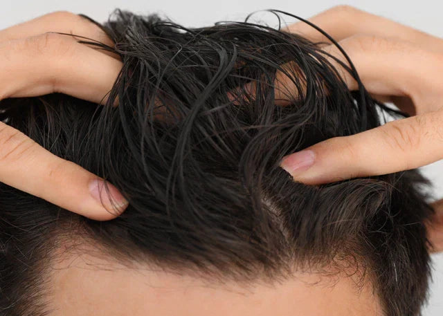 A fair-skinned man touches his volumized black hair in front of a grey background.