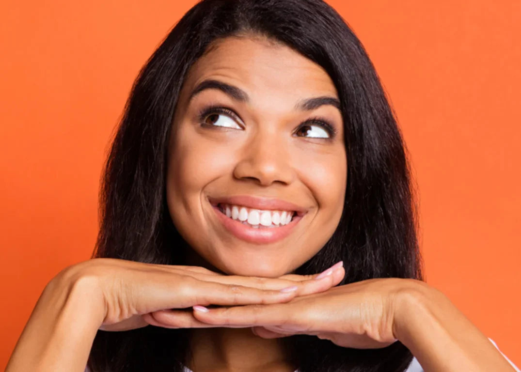 A woman with tan skin and silk pressed hair smiles and looks up in front of an orange background.
