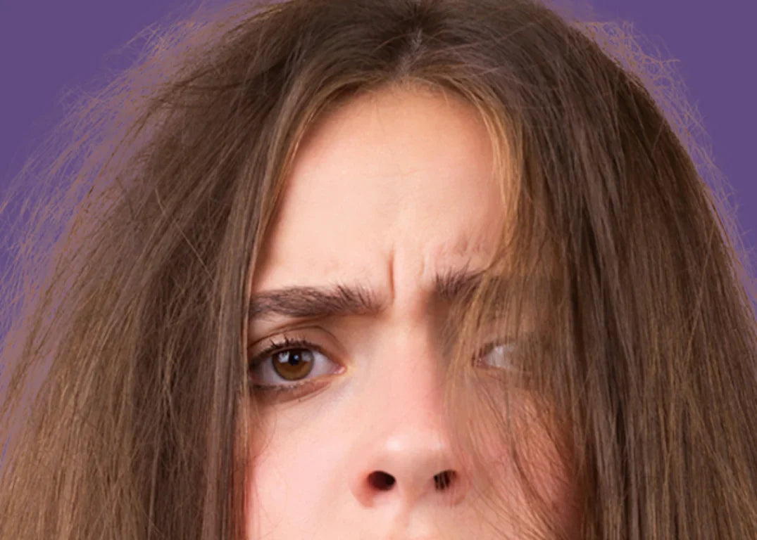 woman with fair skin and frizzy humid brown hair looks confused in front of a purple background.