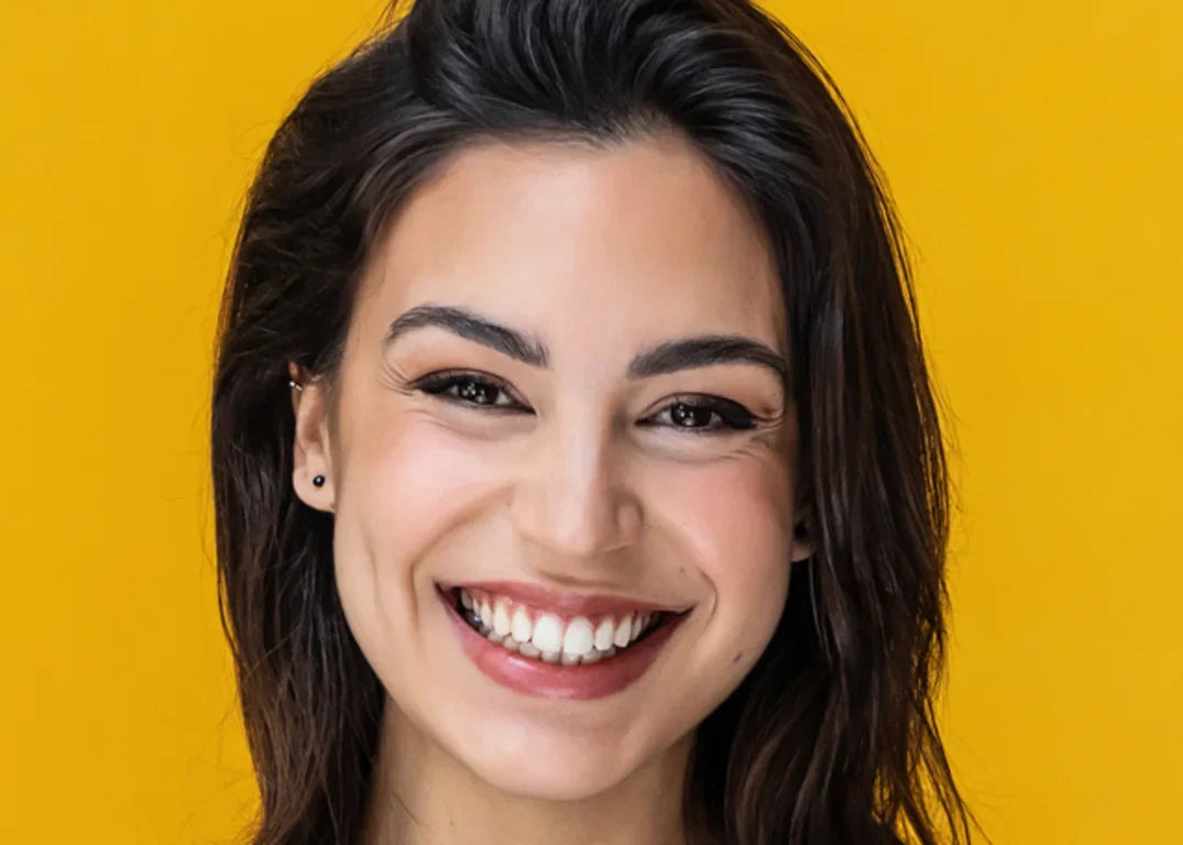 Woman with olive complexion dark eyes and dark hair smiles forward in front of a yellow background.