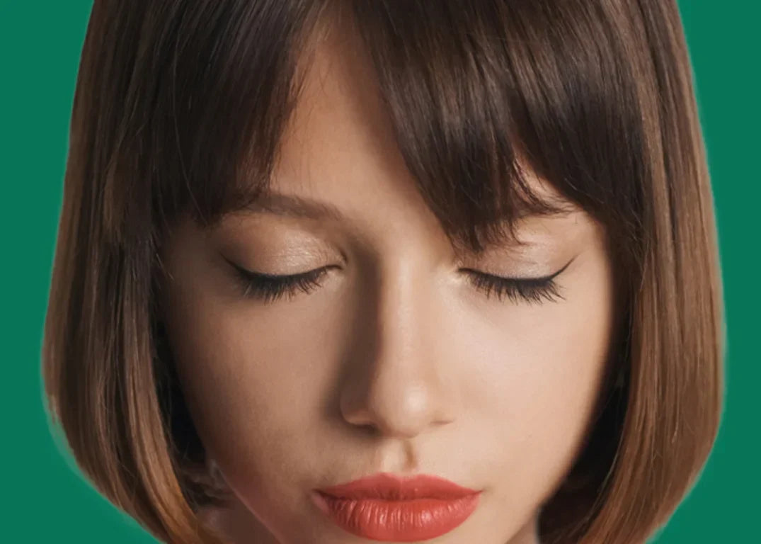 A woman with fair skin and a brown blunt cut bob hairstyle is closing her eyes.