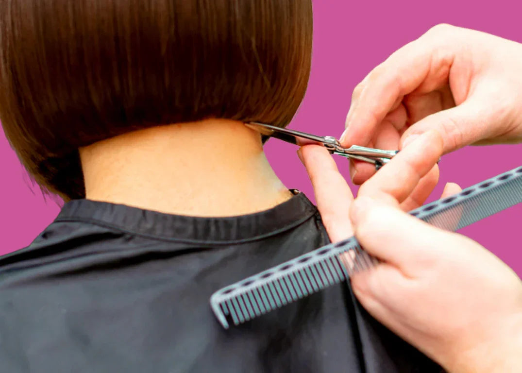 Barber cutting a fair-skinned woman's hair with scissors in front of a pink background, showcasing the best hair styles for thinning hair.