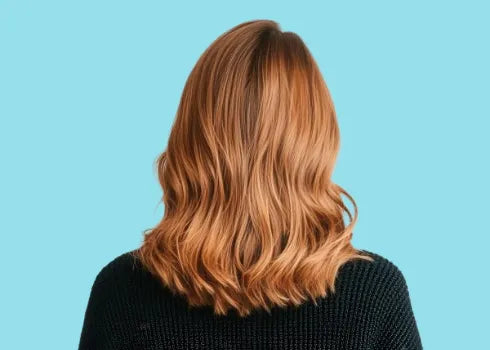 The back of a person with thin wavy, shoulder-length ginger hair, wearing a dark knit sweater, against a light blue background