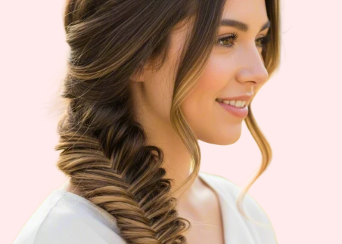 A woman with brown hair styled in a fish tail braid faces away from the camera in front of a pink background