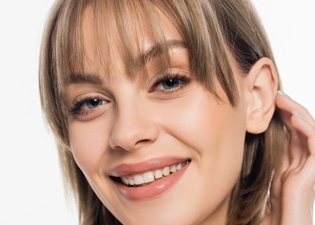 A woman with short higjlighted bangs smiles in front of a white background.