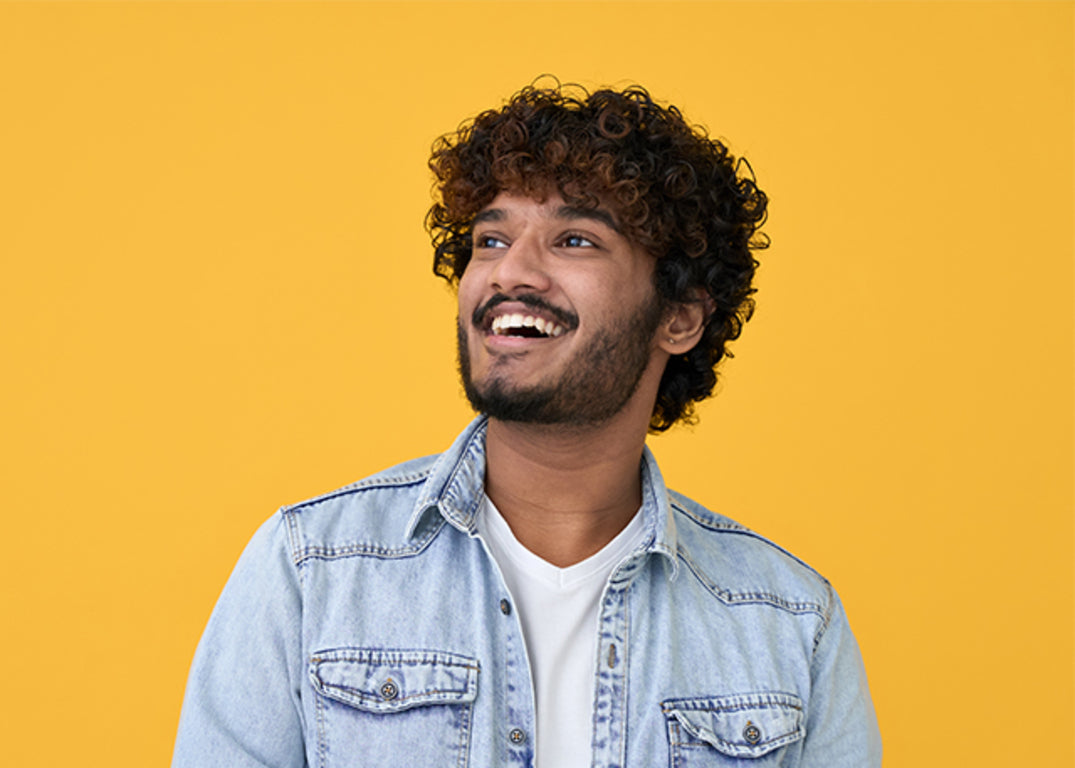 A man with curly hairstyle smiling and looking up while wearing denim shirt.