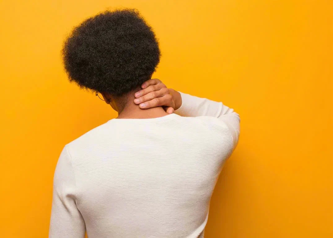 A stressed dark-skinned man with curly black hair has dry scalp and dandruff, in front of an orange background.