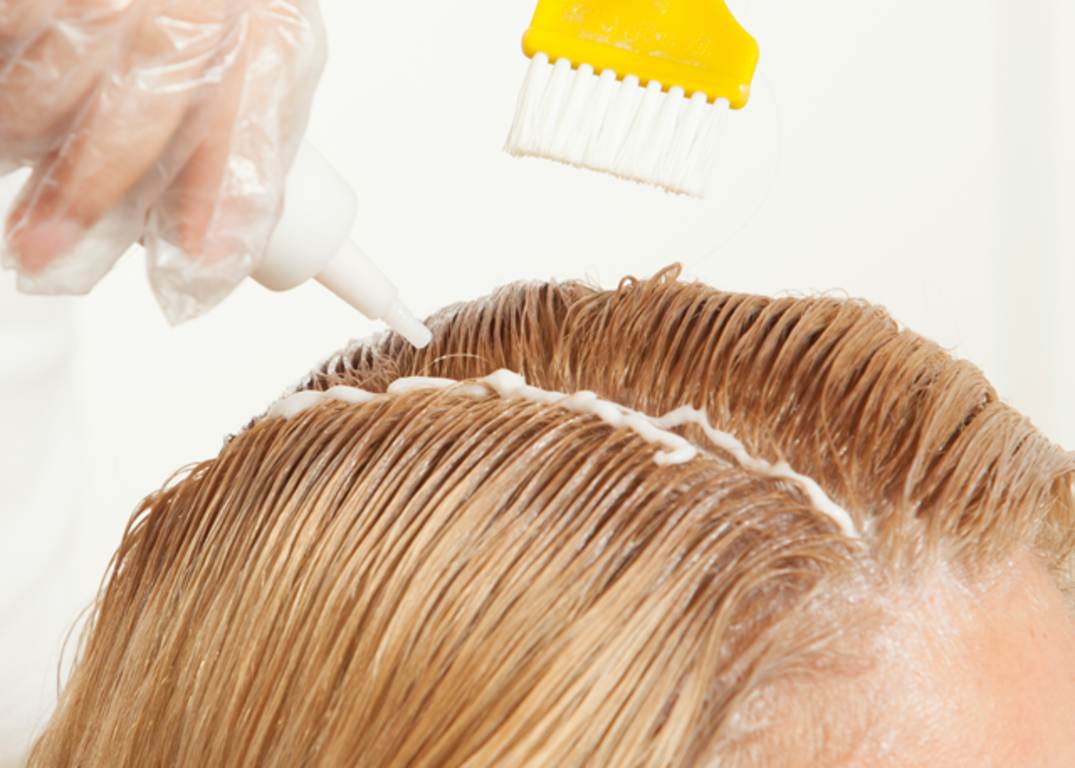 Woman with fair skin and blonde hair has her hair dyed in front of a white background