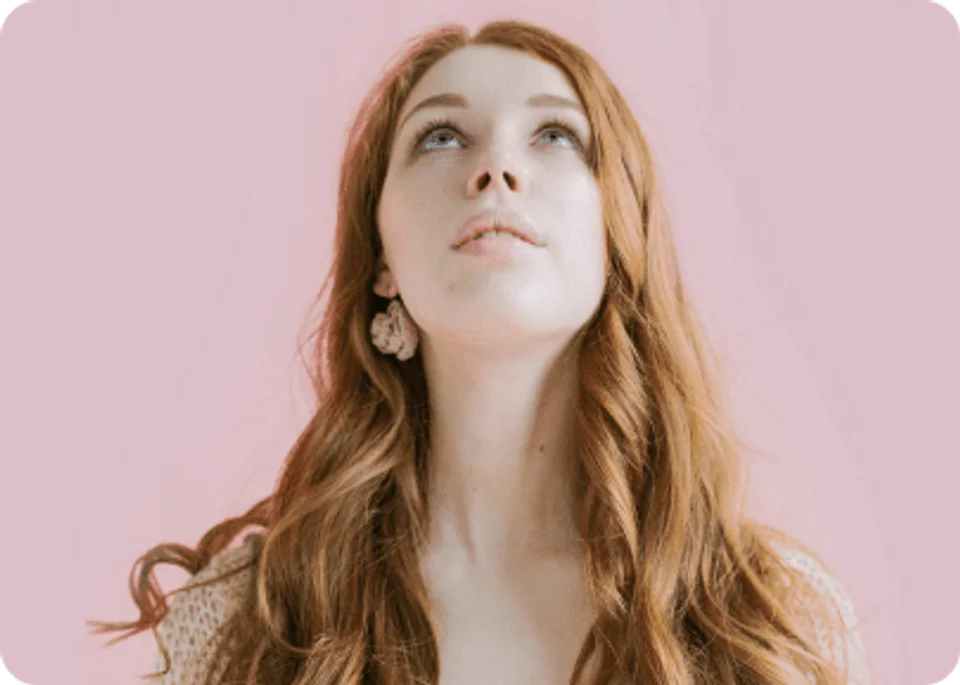 Fair skinned girl with long red hair looking up. Pink background.