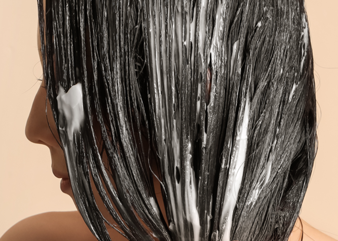 Woman with fair skin facing side has hair coated with conditioner in front of a light brown background