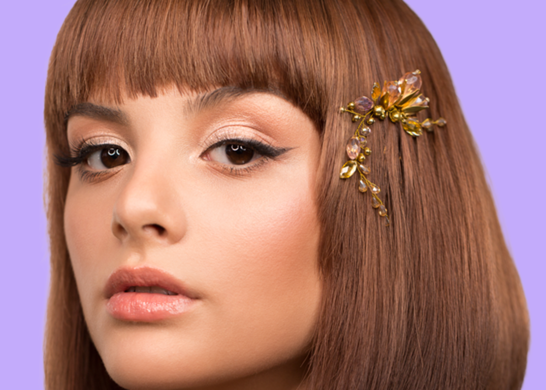 A woman with short brown bangs and a hair clip looks forward in front of a purple background.
