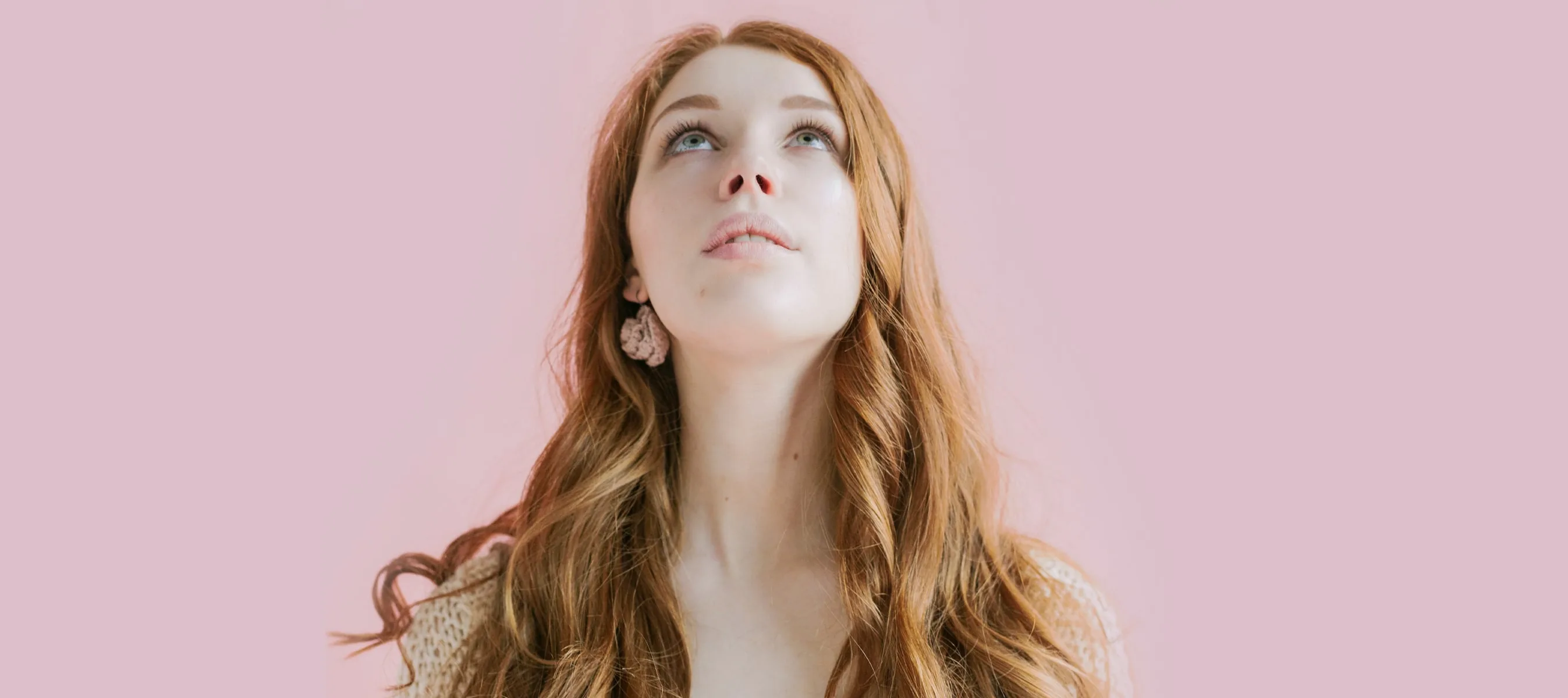 Fair skinned girl with long red hair looking up. Pink background.