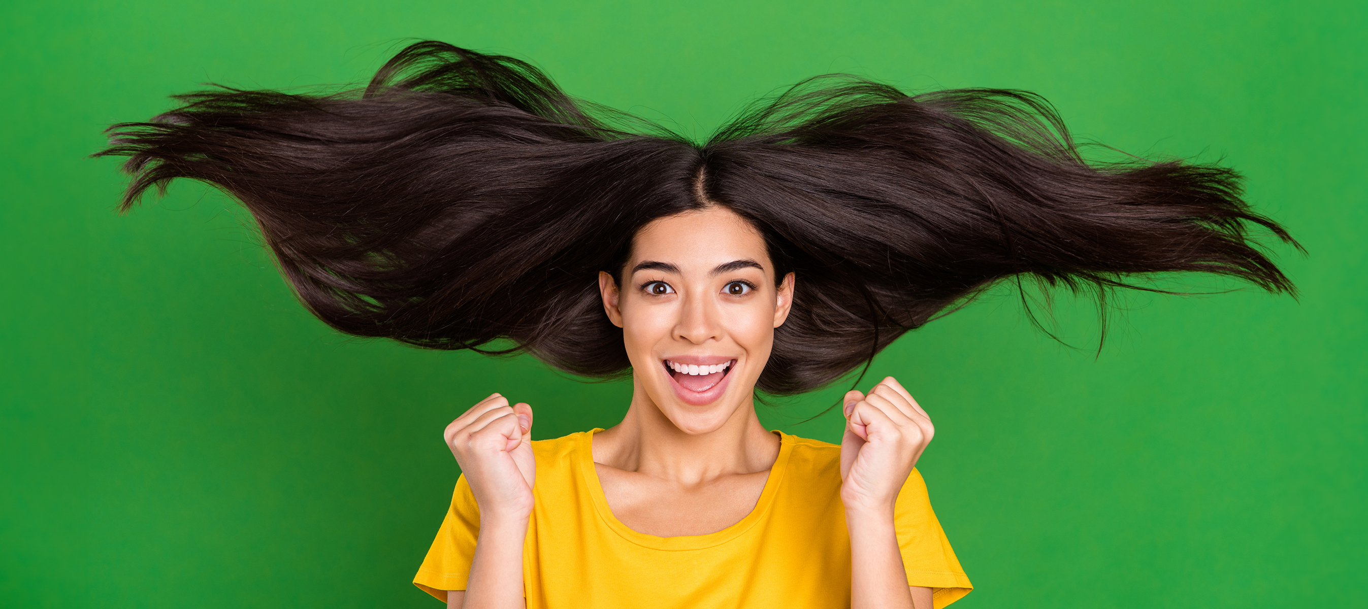 Portrait of girl with long brunette hair gesturing overjoyed with great healthy clean hair isolated on bright green color background