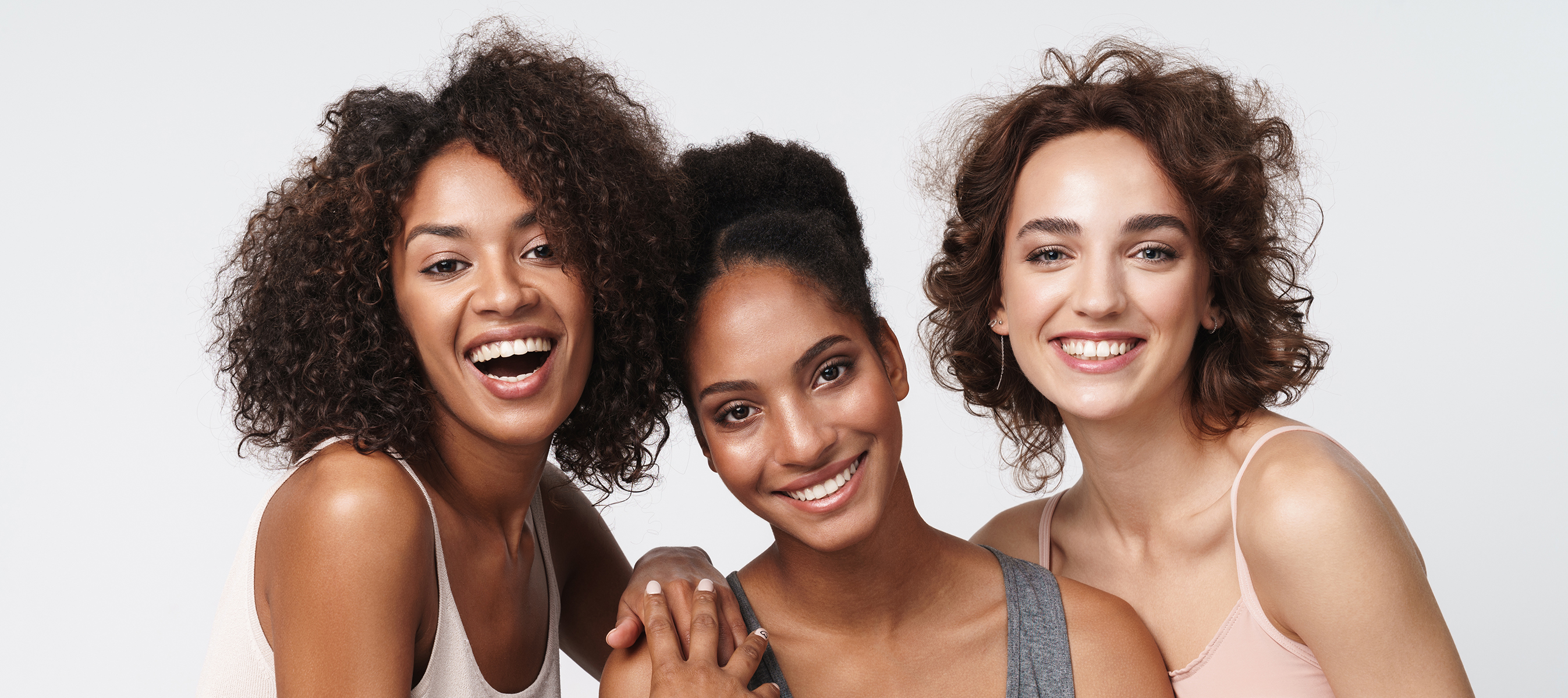 Portrait of three gorgeous multiracial women standing together with a combination of curly and wavy hair and smiling at camera isolated over white background